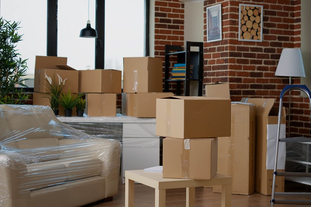 Nobody in empty living room with cardboard packaging at new home, furniture things in stack of carton boxes. No people in household property with package cargo to move in, real estate.