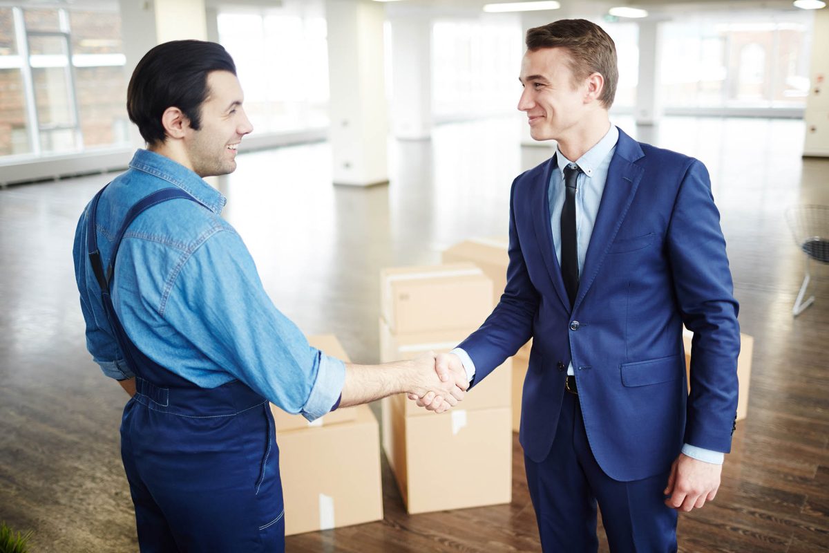 Young businessman in suit and delivery man in uniform handshaking after relocation work