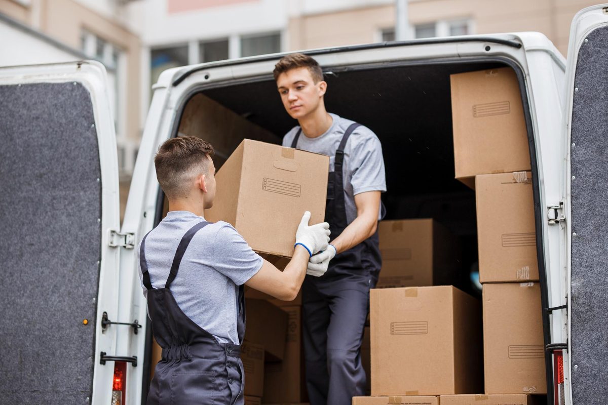 Two young handsome movers wearing uniforms are unloading the van full of boxes. House move, mover service.