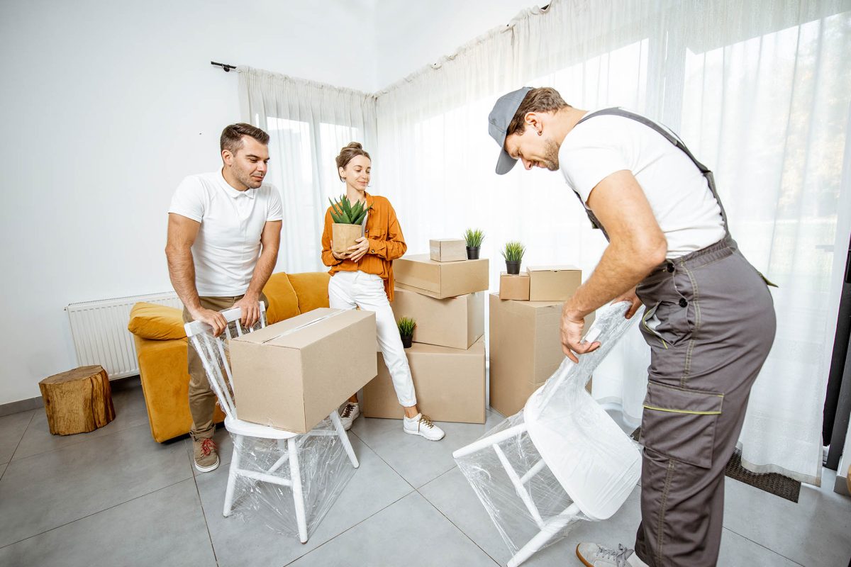 Young couple in the living room of their new home, mover performs professional furniture delivery during the relocation