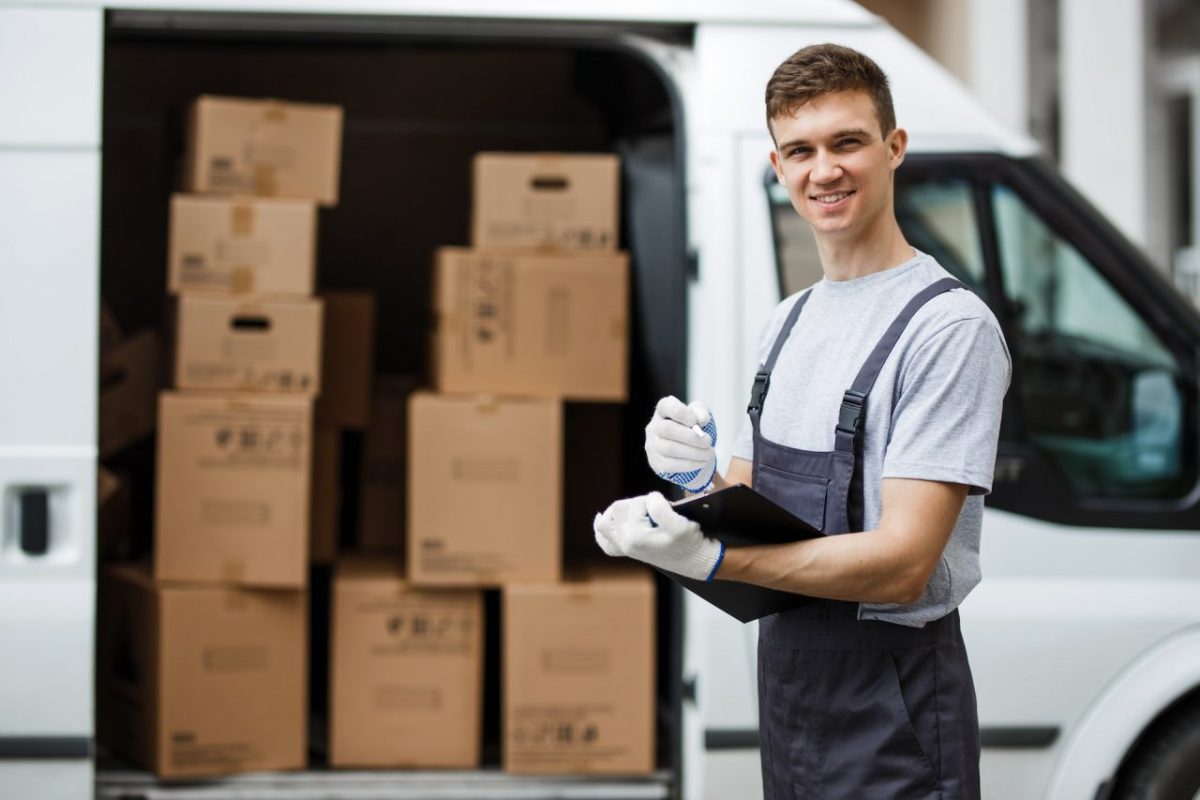 a-young-handsome-smiling-worker-wearing-uniform-is-standing-next-to-the-van-full-of-boxes-holding-a.jpg