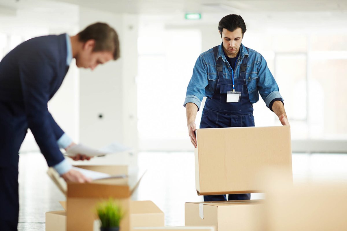 Relocation service worker putting packed box on top of another one while helping to carry packages